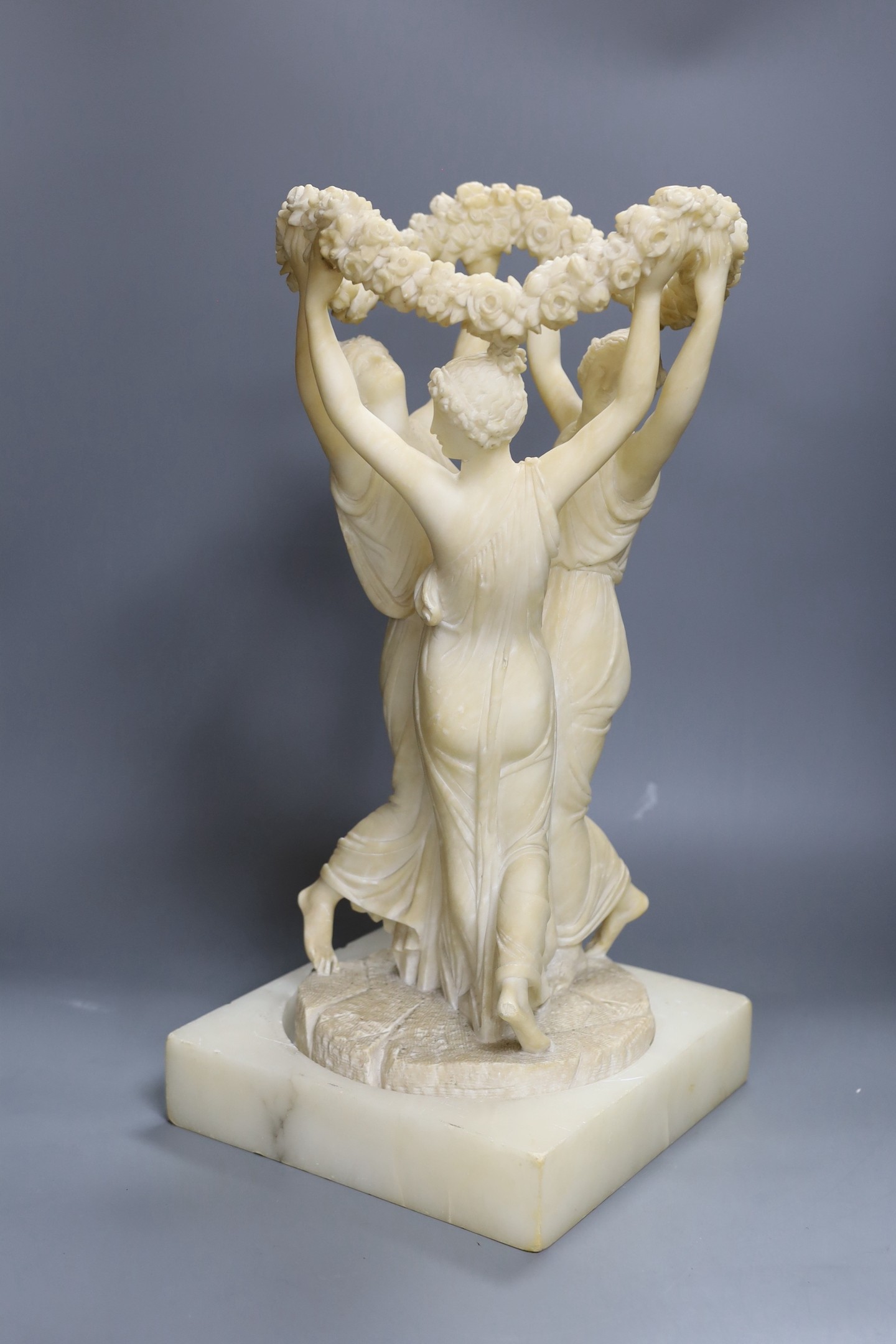 An alabaster carving of the Three Graces on associated base, 47cm total height